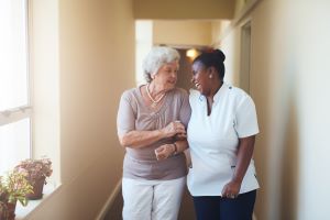 A nurse and a elderly lady is walking down a hall.