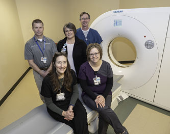 Picture of five imagig dept. staff members standing and sitting near a MRI machine.