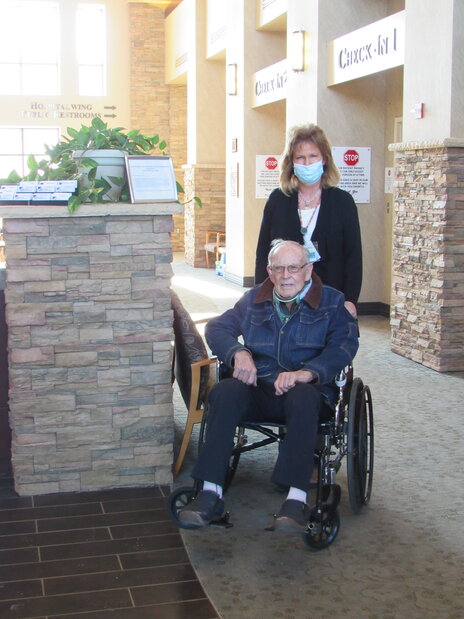 Volunteer standing behind a patient in a wheelchair, outside hospital.